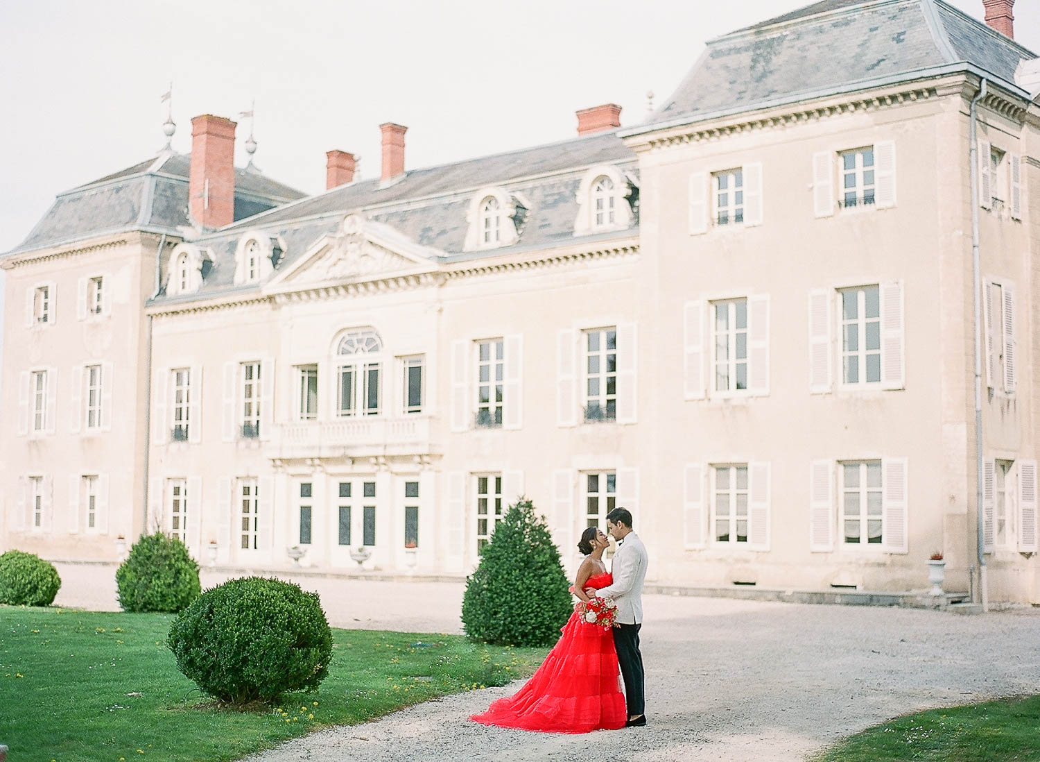 Bride-in-red-monique-lhuillier-dress-and-groom-in-front-of-chateau-de-varennes-hugging